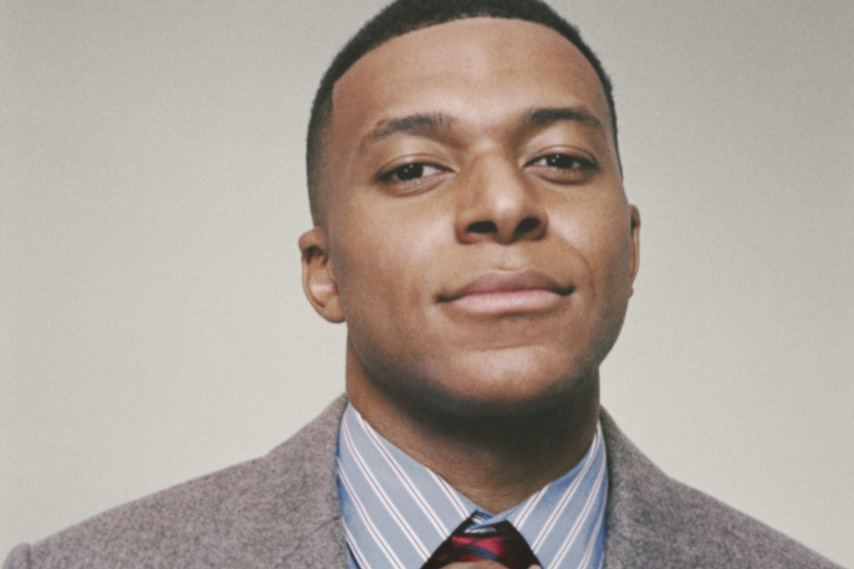 Kylian Mbappé. Zdjęcie nowego ambasadora marki Dior, którego ogłosił Jonathan Anderson. Francuski piłkarz nosi szarą marynarkę w jodełkę, koszulę w błękitno-białe paski oraz krawat w czerwono-granatowe paski.