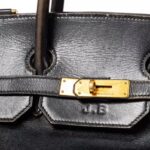 Pierwszy model Hermes Birkin trafi na aukcję w Paryżu. Na zdjęciu zbliżenie na złote zapięcie oraz widoczne logo J.B.