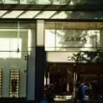 Inditex wyniki finansowe Q1 2025. Zdjęcie sklepu Zara, który należy do hiszpańskiego holdingu Inditex. Widać na nim cień rzucany przez drzewa, wejście i manekiny na wystawie. Na pierwszym planie znajdują się przechodnie.