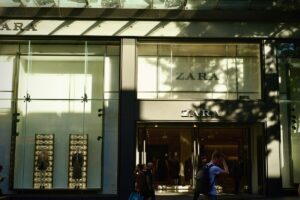 Inditex wyniki finansowe Q1 2025. Zdjęcie sklepu Zara, który należy do hiszpańskiego holdingu Inditex. Widać na nim cień rzucany przez drzewa, wejście i manekiny na wystawie. Na pierwszym planie znajdują się przechodnie.