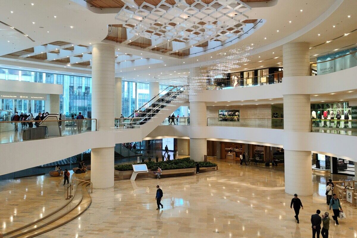 Sadyba Best Mall zamknięcie. Zdjęcie centrum handlowego utrzymanego w stylu nowoczesnym, z dominującą bielą. Na zdjęciu widać trzy piętra galerii, schody ruchome i klientów. Na podłodze odbijają się lampy.