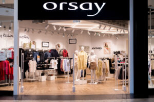 Zdjęcie sklepu Orsay z białą nazwą na czarnym tle. Widać główne wejście oraz manekiny i ubrania na wieszakach. Orsay jest jedną z firm odzieżowych, które zamknęły swoje sklepy w Polsce.