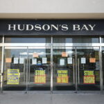 Hudson's Bay Company upadłość. Zdjęcie zamykającego się sklepu Hudson's Bay w Kanadzie. Na zdjęciu szyld z nazwą oraz szklane drzwi oklejone reklamami zachęcającymi do zakupu rzeczy z wyprzedaży.