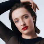 Iga Świątek na pierwszym miejscu rankingu Forbes Women - 100 Najcenniejszych Kobiecych Marek Osobistych 2025. Na zdjęciu Iga Świątek w kampanii Lancome, ubrana w czarne dopasowane body. Rękę trzyma na głowie. Ma czerwone usta i delikatny makijaż.