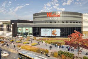 Kładka przy Galerii Mokotów zniknie po 25 latach. Na zdjęciu duże centrum handlowe o nazwie 'Westfield Mokotów' z nowoczesną architekturą: zakrzywiona fasada w odcieniach szarości i czerni, duże szklane witryny. Na budynku wyróżnia się czerwone logo 'Westfield'.
