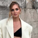 Chiara Ferragni likwiduje firmę. Zdjęcie włoskiej influencerki w spiętych włosach z luźno puszczonym pasemkiem przy twarzy i mocnym makijażu wieczorowym. Kobieta nosi kremową marynarkę o mocno oversizowym kroju. Pod nią ma czarny stanik. Stoi na tle muru.