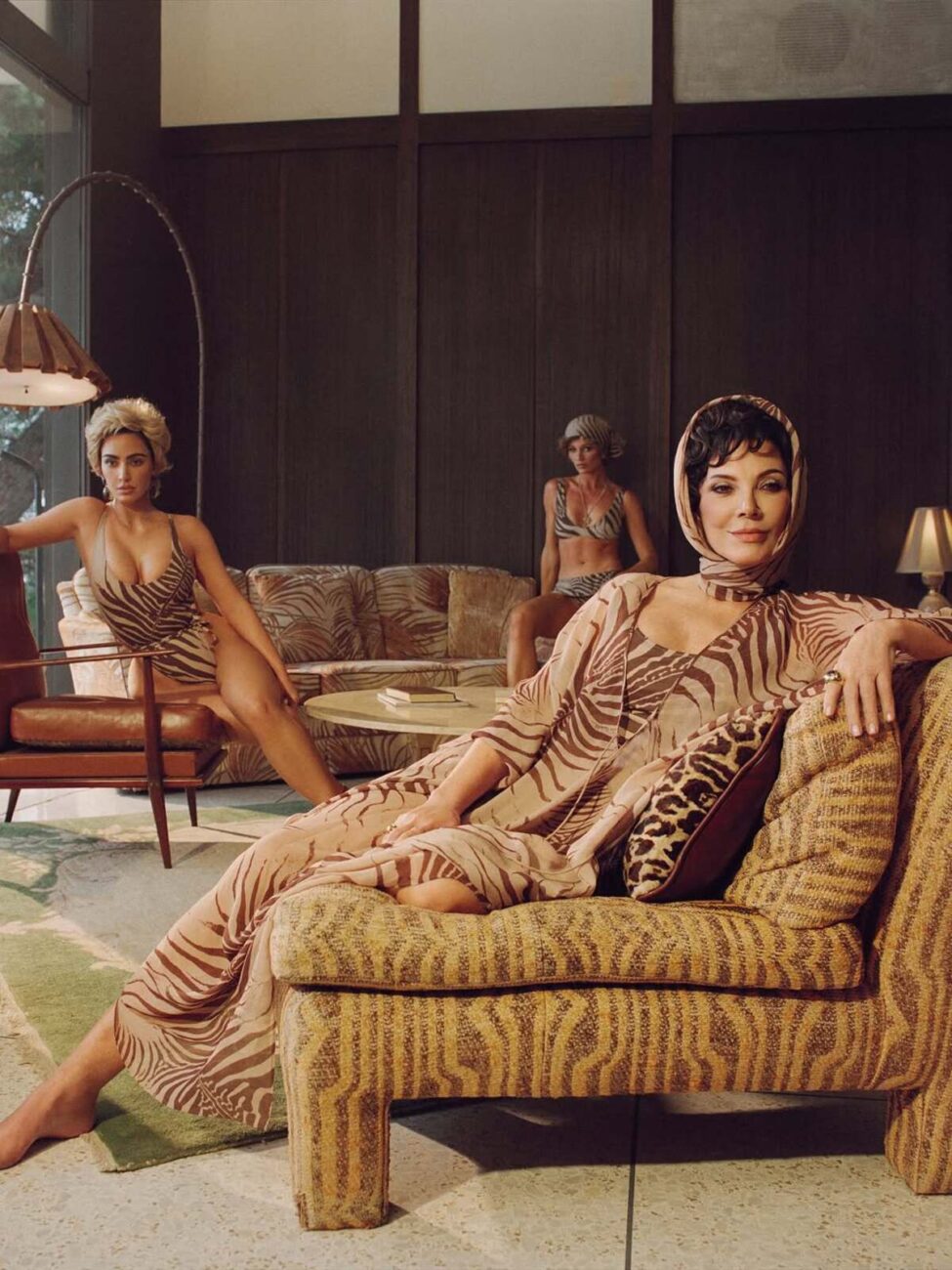 Zdjęcie promujące kampanię Roberto Cavalli x SKIMS, na którym pozuje Kris Jenner w zwiewnej sukience w motyw zebry. Za nią w tle siedzi Kim Kardashian, a dalej jeszcze jedna modelka. Kobiety pozują w pomieszczeniu stylizowanym na estetykę retro.