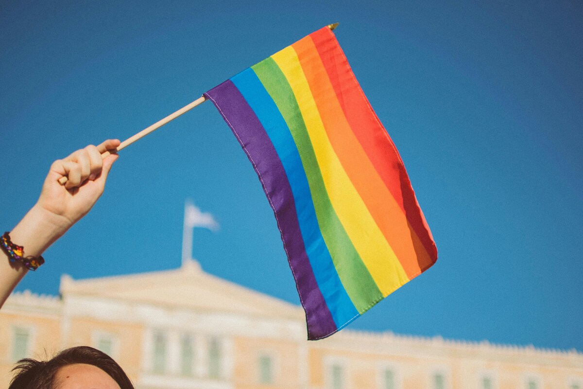 Zdjęcie tęczowej flagi na tle budynku i niebieskiego nieba. To symbol społeczności LGBTQ+, która w czerwcu obchodzi Miesiąc Dumy (Pride Month).