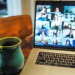 Laptop i kubek kawy obok. Na ekranie widoczny webinar.