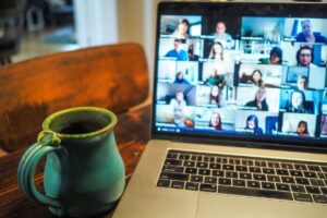 Laptop i kubek kawy obok. Na ekranie widoczny webinar.