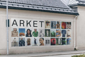 Zdjęcie promujące drugi sklep ARKET w Warszawie, przedstawiające baner reklamowy zawieszony na budynku. Widać na nim wiele zdjęć modelek, modeli i produktów. To zapowiedź trzeciego sklepu ARKET w Polsce.