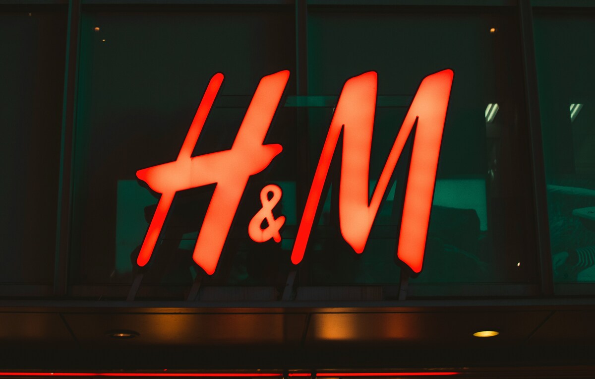 Płatne zwroty w H&M. Zdjęcie czerwonego logo H&M w formie podświetlanego szyldu. Zdjęcie wykonano wieczorem.
