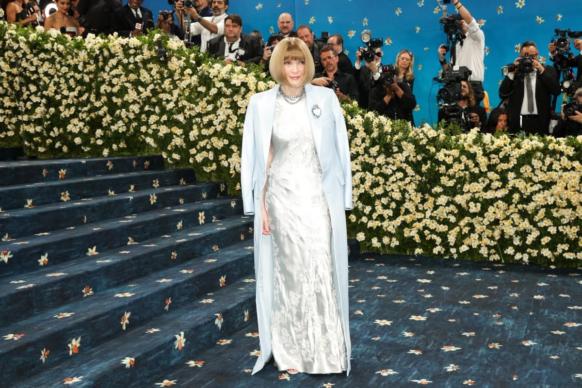 Met Gala 2026 – Beyonce, Nicole Kidman i Serena Williams poprowadzą galę z Anną Wintour. Na zdjęciu: Anna Wintour podczas Met Gala pozuje na kultowych schodach The Met w Nowym Jorku. Ma na sobie elegancką, srebrzystą satynową suknię z haftem i długi błękitny płaszcz, a w tle widać ścianę z kwiatów oraz tłum fotoreporterów. Ikona świata mody tradycyjnie otwiera najważniejsze wydarzenie branży.