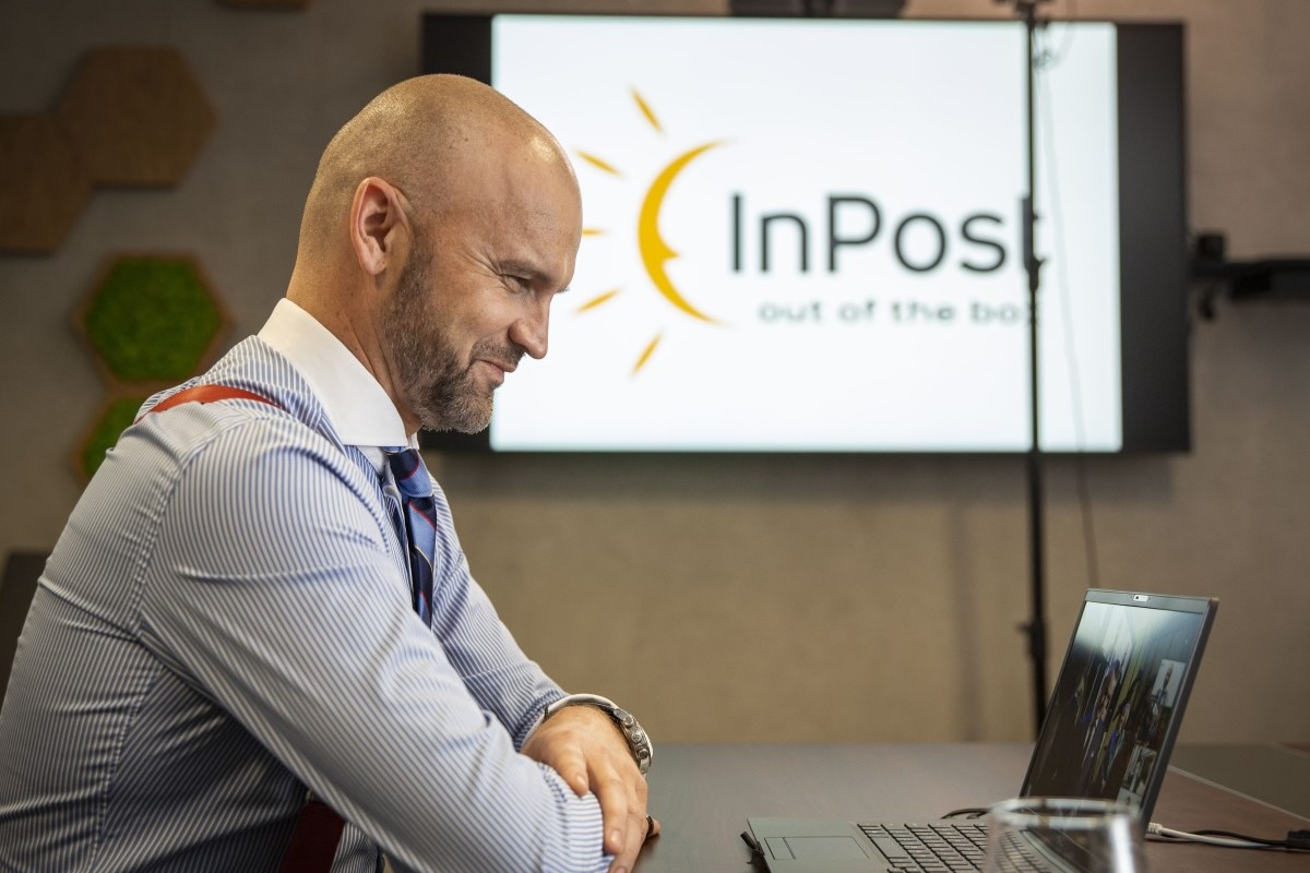 Czy InPost pozostanie polski po sprzedaży. Na zdjęciu Rafał Brzoska, CEO InPost siedzi wpatrzony w laptopa. W tle prezentacja z dużym logo InPost.