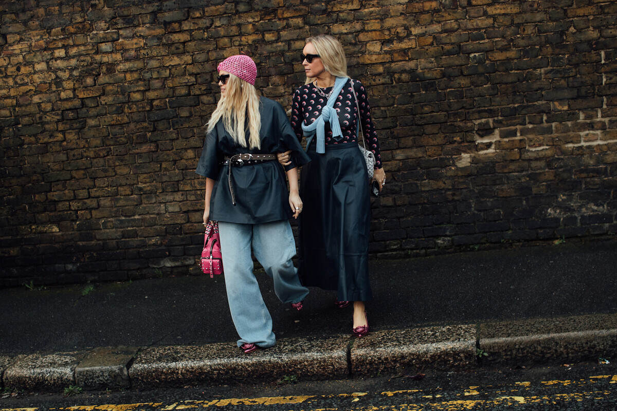 CO2 zamieniane w tkaniny, ubrania z dwutlenku węgla. Dwie kobiety w stylowych, miejskich stylizacjach idą ulicą na tle ceglanego muru, prezentując nowoczesne podejście do mody. Zdjęcie symbolicznie nawiązuje do zmian w branży fashion, która coraz częściej sięga po innowacyjne i bardziej zrównoważone materiały. W kontekście artykułu pokazuje kierunek, w którym moda może ewoluować dzięki technologiom wykorzystującym CO2.