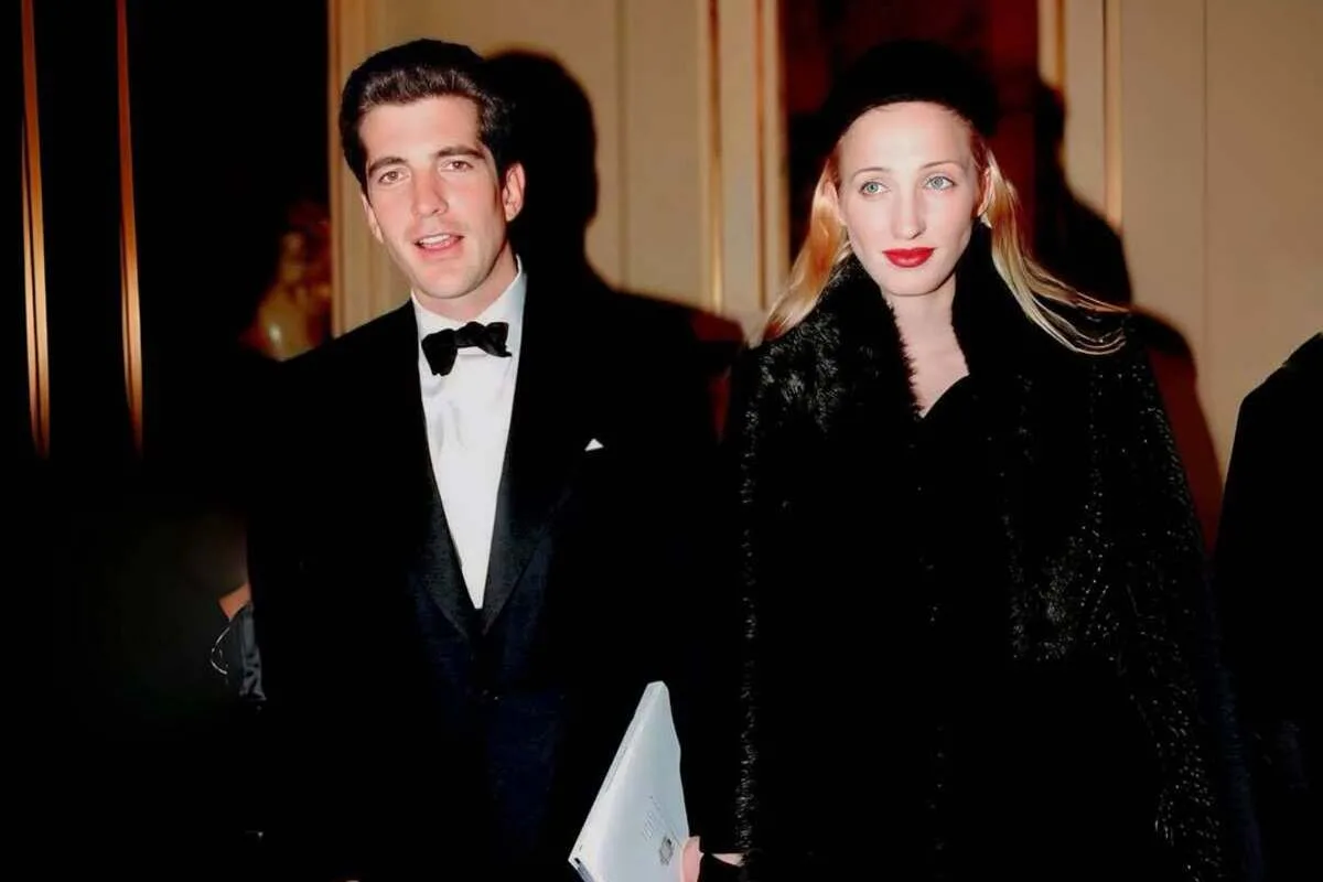Efekt Carolyn Bessette-Kennedy. Na zdjęciu: John F. Kennedy Jr. i Carolyn Bessette-Kennedy podczas oficjalnego wydarzenia w latach 90. Carolyn ma na sobie minimalistyczną stylizację z czarnym płaszczem, charakterystyczną dla jej eleganckiego stylu.
