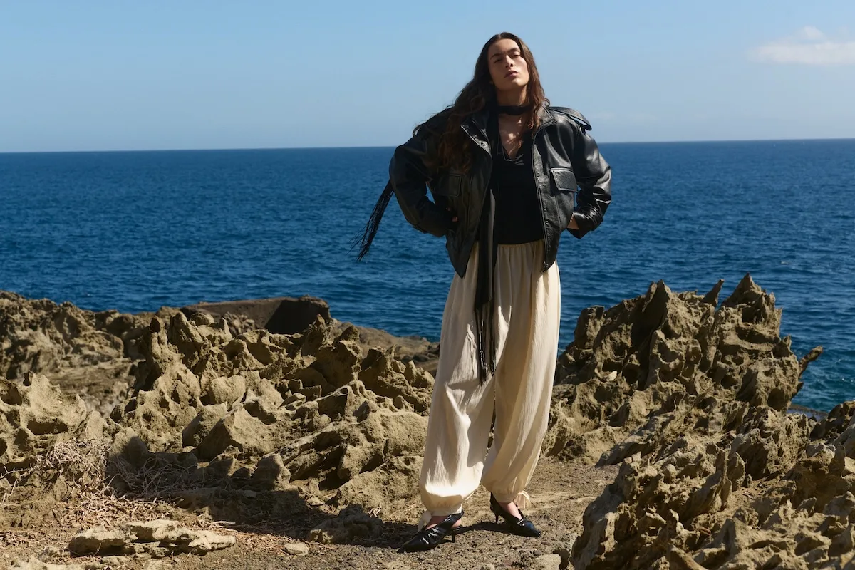 Modelka w czarnej skórzanej kurtce i jasnych spodniach na skalistym wybrzeżu – kampania Reserved wiosna–lato 2026