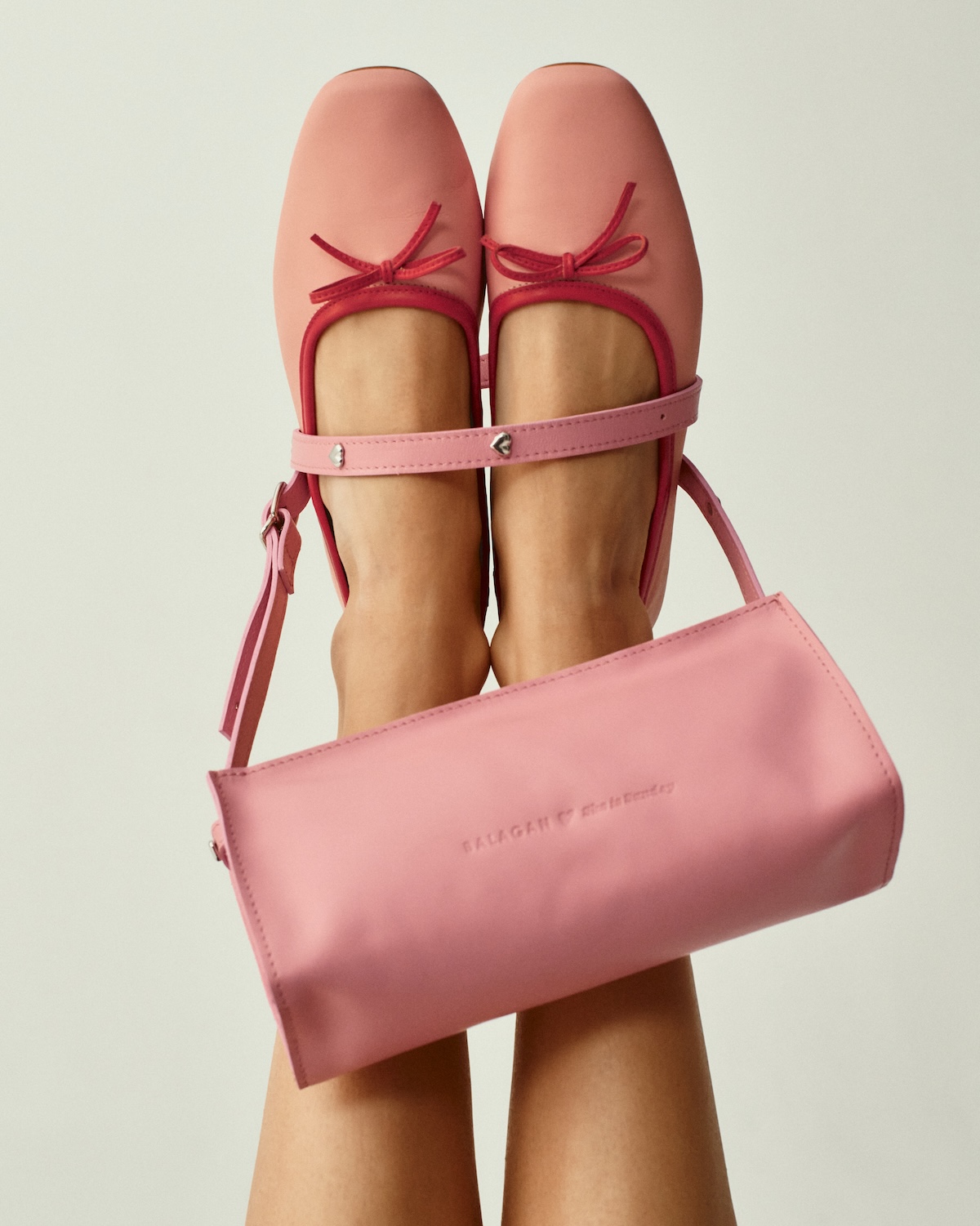 Zbliżenie na różowe baleriny z kokardką oraz torebkę z kolekcji Balagan x She is Sunday. Delikatna kolorystyka podkreśla kobiecy i subtelny charakter projektu. Minimalistyczne tło eksponuje detale i formę dodatków.
