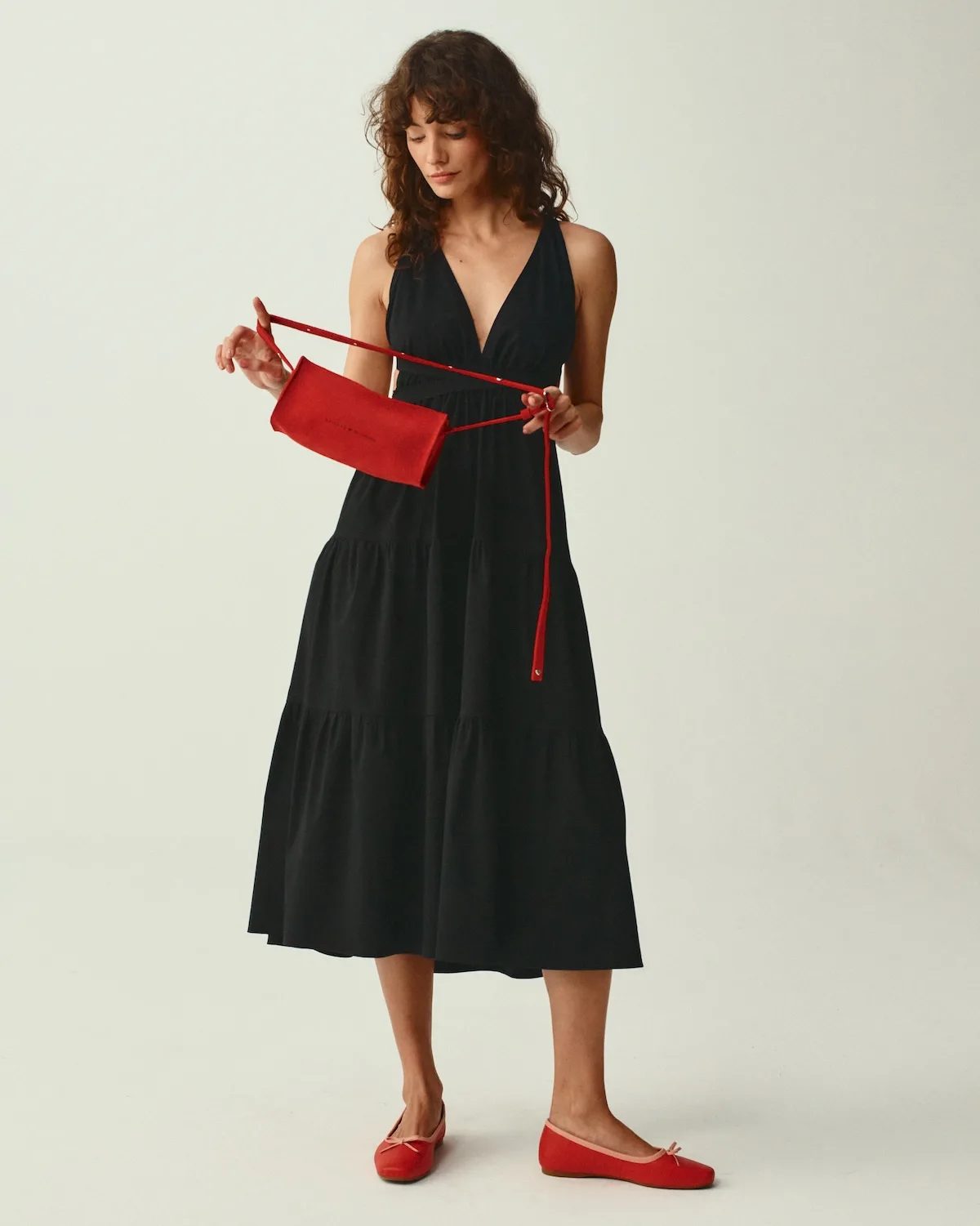 Modelka w czarnej sukience prezentuje czerwoną torebkę z kolekcji Balagan x She is Sunday. Kontrast między klasyczną stylizacją a intensywnym dodatkiem przyciąga uwagę. Całość podkreśla uniwersalność i elegancję projektu.