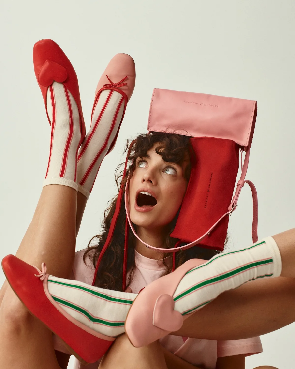 Modelka w dynamicznej pozie prezentuje baleriny i torebki z kolekcji Balagan x She is Sunday. Zestawienie czerwieni i różu buduje energetyczny, nowoczesny charakter stylizacji. Zdjęcie oddaje lekkość i zabawny ton całej współpracy.