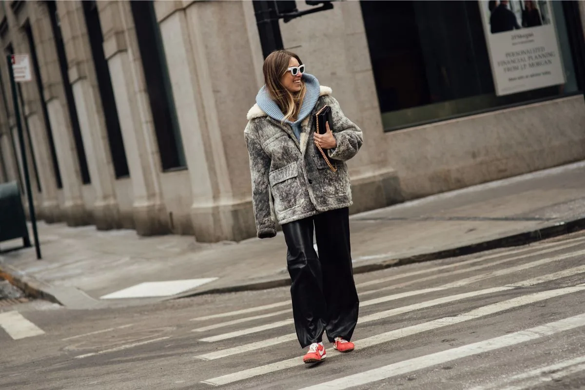 Kobieta w miejskiej stylizacji przechodzi przez ulicę w oversize’owej kurtce typu shearling, szerokich spodniach i wyrazistych sneakersach. Styl odzwierciedla kierunek widoczny w Farfetch Index 2026 – połączenie komfortu, funkcjonalności i rozpoznawalnych elementów. To przykład „codziennego luksusu”, w którym kluczową rolę odgrywają praktyczne, ale charakterystyczne produkty.
