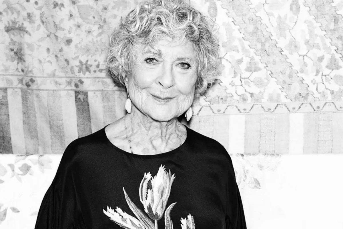 Czarnobiały portret Joan Burstein, założycielki butiku Browns, jednej z najważniejszych postaci w historii retailu modowego. Elegancka sylwetka i spokojny uśmiech oddają jej charakterystyczny styl oraz wieloletnie doświadczenie w odkrywaniu talentów w branży fashion.