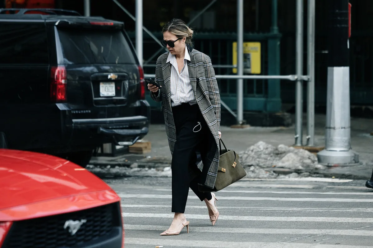 Kobieta korzysta ze smartfona podczas przechodzenia przez ulicę w trakcie L4 – sytuacja, która może zostać sprawdzona przez ZUS w kontekście pracy zarobkowej. W 2026 roku kontrole zwolnień lekarskich są bardziej szczegółowe, a każda aktywność może wpłynąć na prawo do zasiłku chorobowego.