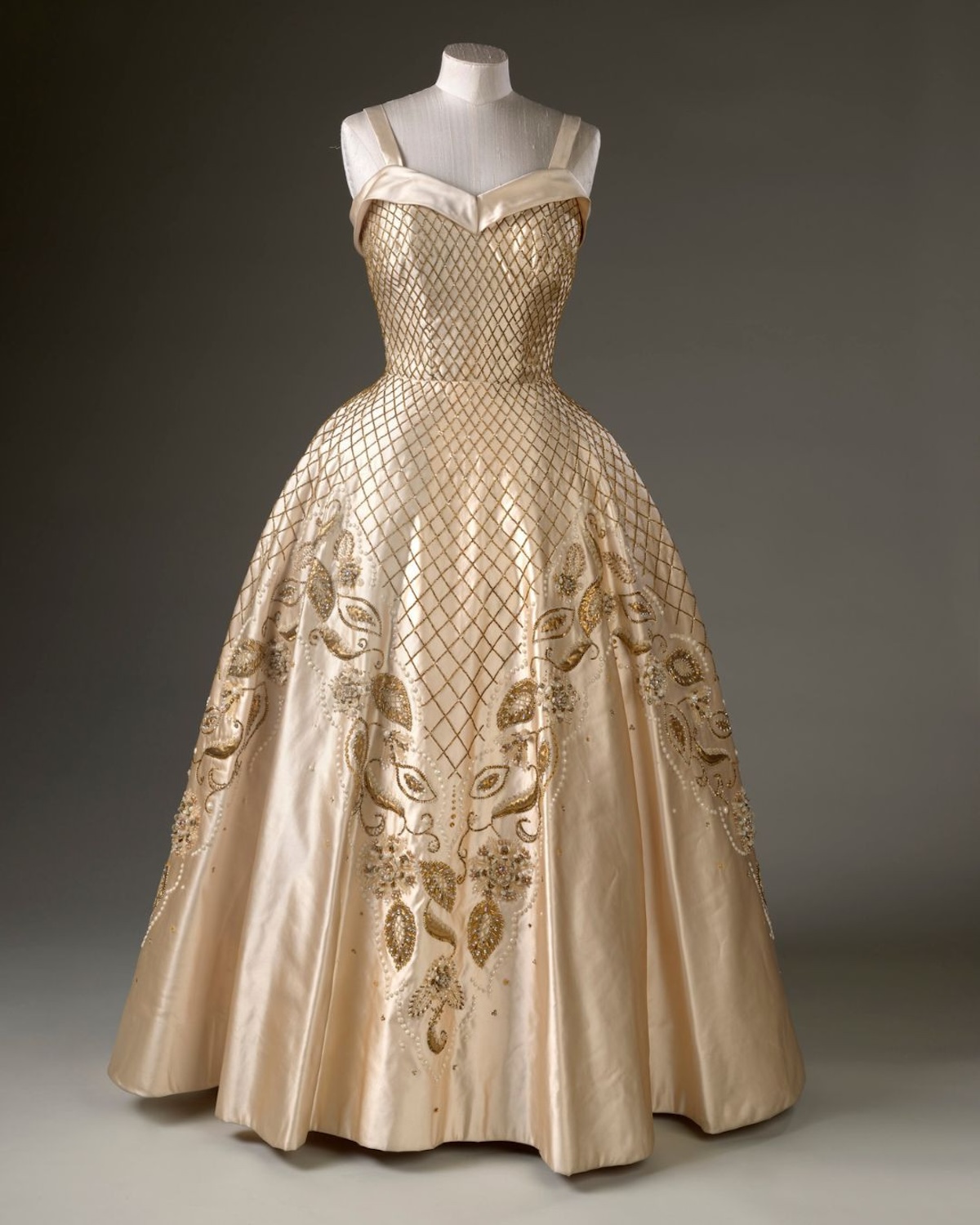 Fragment archiwalnej stylizacji królowej Elżbiety II – widoczny detal tkaniny i konstrukcji sukni podkreśla kunszt projektantów współpracujących z monarchinią. Tego typu elementy, pokazywane na wystawie w Pałacu Buckingham, odsłaniają zaplecze powstawania królewskich kreacji i ich znaczenie w budowaniu wizerunku.