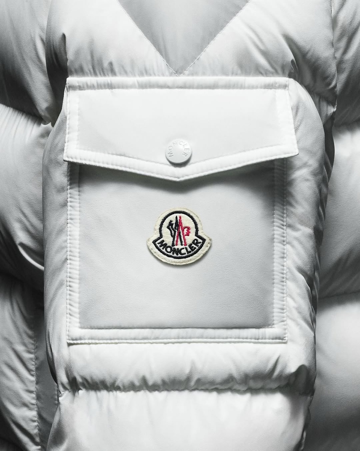 Detal białej puchowej kurtki z logo Moncler podkreśla znaczenie rozpoznawalnych elementów w nowoczesnym luksusie. Modele takie jak Moncler Maya regularnie pojawiają się w Farfetch Index 2026 jako jedne z najczęściej wyszukiwanych. To przykład produktu, który łączy funkcjonalność z silną identyfikacją wizualną.