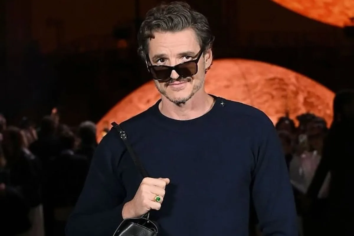 Pedro Pascal ambasador Chanel. Na zdjęciu: Pedro Pascal na pokazie Chanel w Paryżu w eleganckiej, minimalistycznej stylizacji. Aktor ma na sobie granatowy sweter, czarne spodnie i luksusową torbę, uzupełniając look okularami przeciwsłonecznymi. Stylizacja odzwierciedla współczesne podejście Chanel do mody męskiej.
