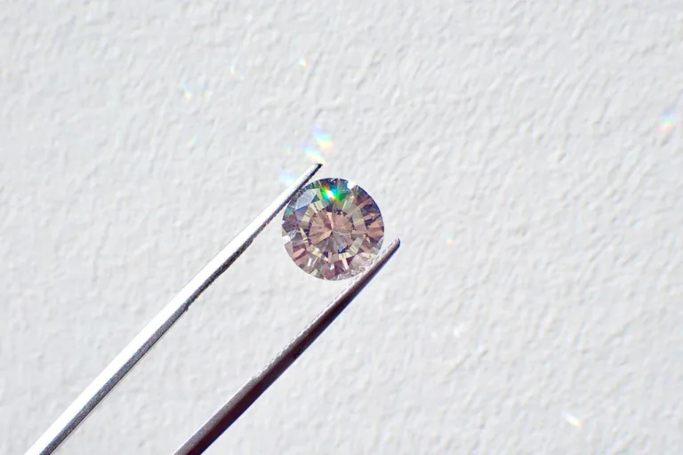 Rynek diamentów 2026. Diament o szlifie brylantowym trzymany w pęsecie na jasnym tle, odbijający światło i tworzący kolorowe refleksy.
