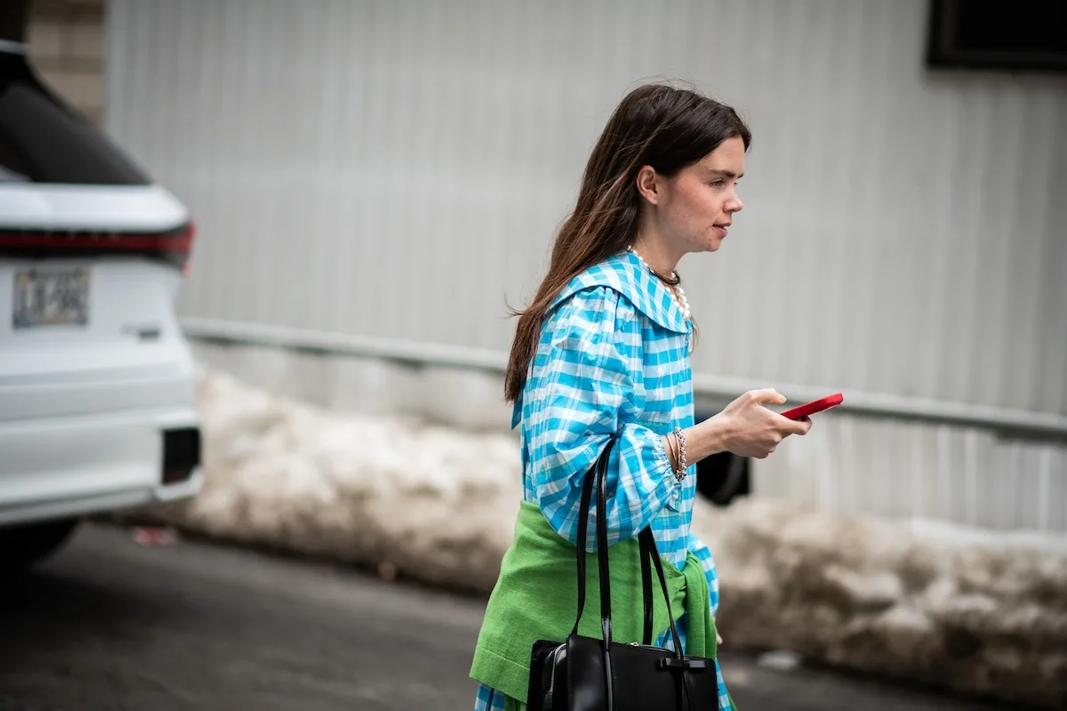 Kobieta w kolorowym outficie korzystająca ze smartfona podczas spaceru po mieście – symbol rosnącej roli social commerce w fast fashion. Zakupy modowe coraz częściej odbywają się online i są inspirowane mediami społecznościowymi. Obraz pokazuje, jak technologia i trendy wpływają na rozwój rynku fast fashion.