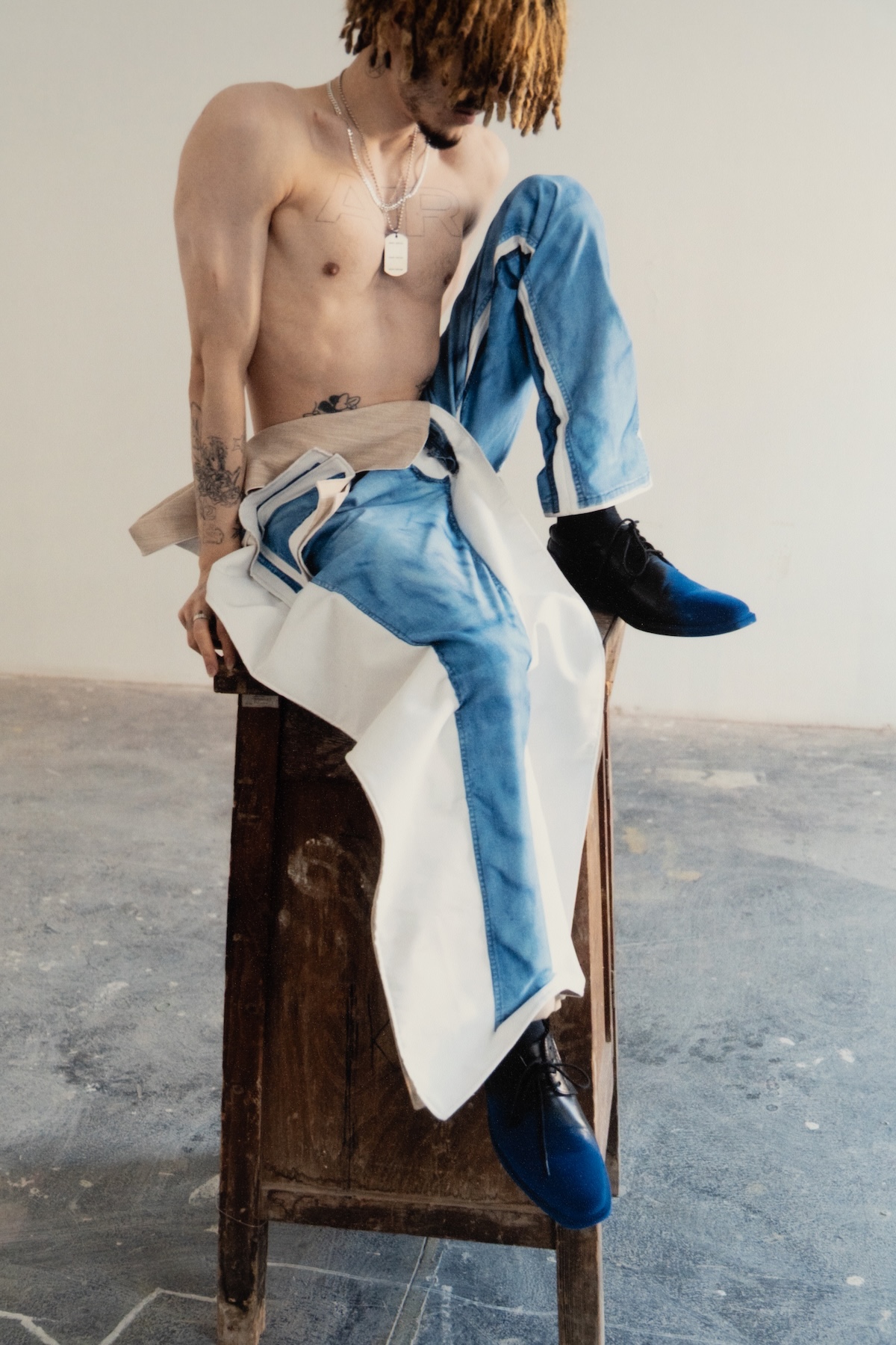 Zbliżenie na modela siedzącego na krześle, widoczne detale patchworkowych spodni projektu Jana Anusza.