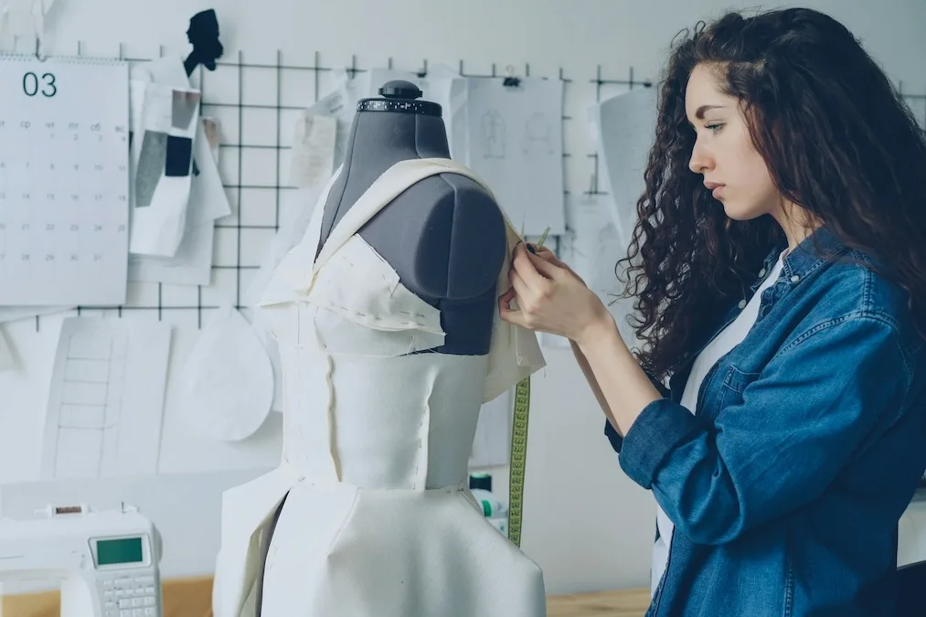 Projektantka dopasowująca suknię na manekinie w pracowni krawieckiej podczas tworzenia kolekcji. Specjaliści z praktycznymi umiejętnościami konstrukcji i szycia są coraz bardziej poszukiwani, co stopniowo wpływa na wzrost ich wynagrodzeń.