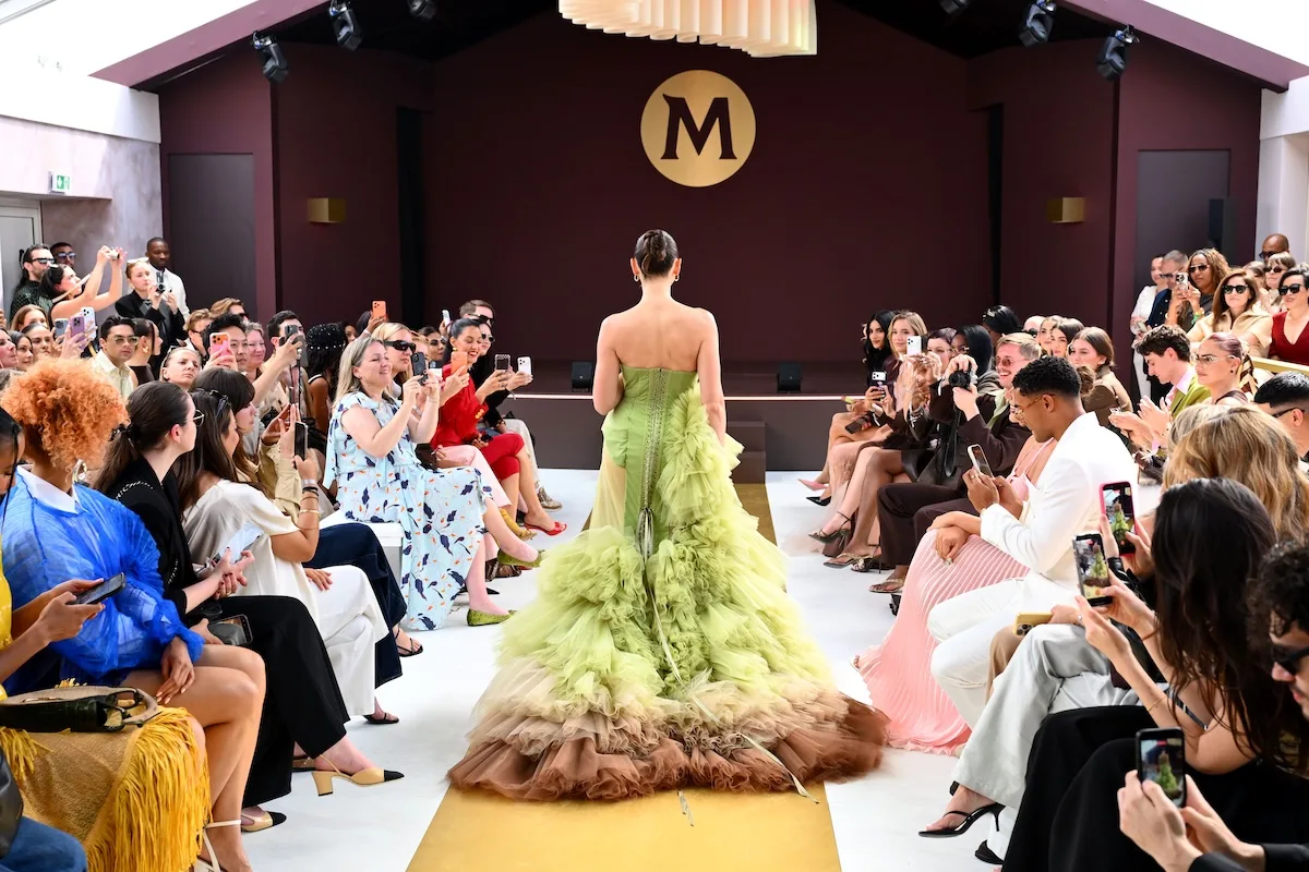 Widok na wybieg House of Magnum w Cannes z modelką w zielonej sukni oraz publicznością fotografującą pokaz.
