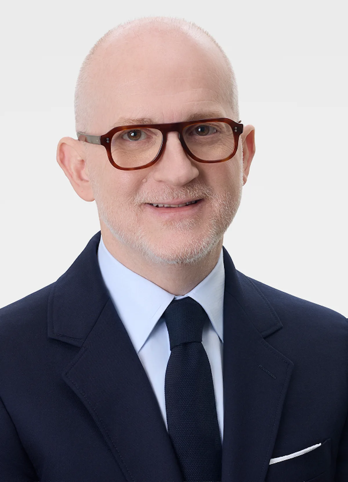 Portret Joshuy Schulmana, CEO Burberry, w granatowym garniturze i okularach. Menedżer stoi na czele planu naprawczego marki, a nowy system premiowy może podnieść jego wynagrodzenie nawet do 12,2 mln funtów w ciągu trzech lat.