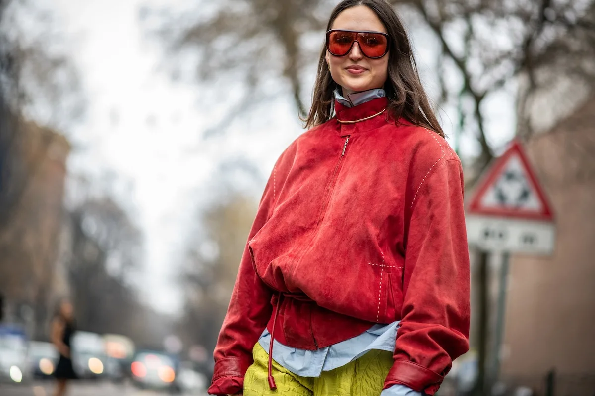 Wyniki finansowe LPP Q1 2026. Kobieta w czerwonej kurtce i dużych okularach przeciwsłonecznych prezentuje nowoczesną stylizację streetwearową na miejskiej ulicy. Zdjęcie nawiązuje do rynku fashion i segmentu modowego premium, w którym działa LPP wraz z markami Reserved, House czy Sinsay. Mimo trudniejszego początku 2026 roku i słabszej sprzedaży kolekcji wiosna-lato, właściciel Reserved kontynuuje ekspansję i rozwój sieci sklepów w Europie.