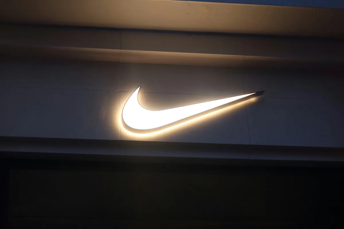 Podświetlane logo Nike umieszczone na elewacji sklepu sportowego po zmroku. Charakterystyczny znak marki wyróżnia się na tle ciemnej fasady budynku.