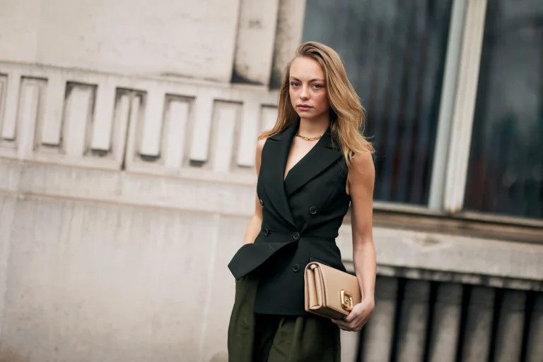 Elegancka kobieta w nowoczesnej stylizacji stoi na tle miejskiej architektury, trzymając minimalistyczną torebkę. Jej profesjonalny wizerunek dobrze wpisuje się w temat zmian na rynku pracy, takich jak nowe zasady stażu pracy 2026, które mogą wpłynąć na karierę i benefity pracowników. Zdjęcie oddaje klimat współczesnego środowiska zawodowego i dynamicznych przemian w zatrudnieniu.