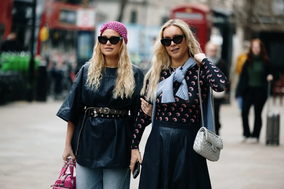 Program poleceń Vinted. Dwie kobiety w stylizacjach street style spacerują po mieście, prezentując modę z drugiego obiegu i codzienny look inspirowany trendami resale. Zdjęcie nawiązuje do rosnącej popularności platform takich jak Vinted oraz aktywności użytkowników, którzy sprzedają i kupują ubrania online. Tego typu stylizacje często trafiają na sprzedaż w aplikacjach second hand, wspierając rozwój programów poleceń i społeczności.