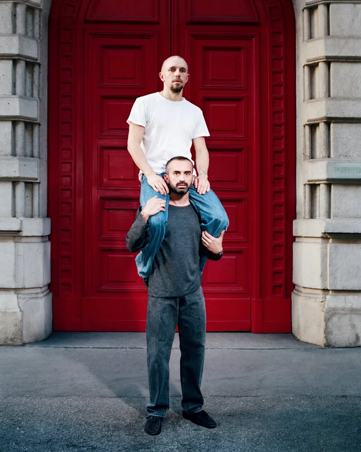 Loris Messina i Simone Rizzo pozują przed czerwonymi drzwiami siedziby Moschino w Mediolanie. Współzałożyciele Sunnei obejmują funkcję nowych dyrektorów kreatywnych włoskiego domu mody. Ich nominacja otwiera kolejny rozdział Moschino po odejściu Adriana Appiolazy.