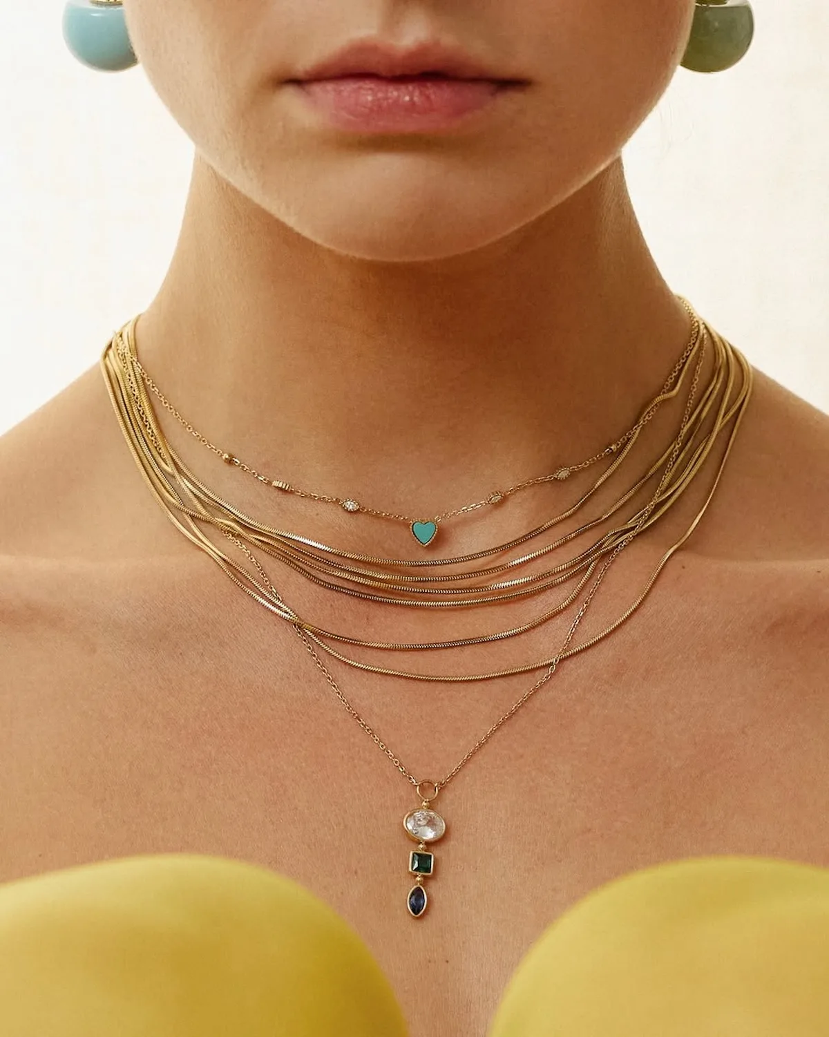 Zbliżenie na złote naszyjniki ZAG Bijoux noszone warstwowo, z kolorowymi zawieszkami i minimalistycznymi detalami. Marka otworzy swój pierwszy sklep w Polsce w warszawskich Złotych Tarasach.