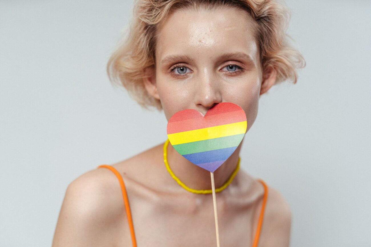 Marki na Pride Month 2026 – portret osoby trzymającej przed twarzą papierowe serce w kolorach tęczowej flagi. Zdjęcie symbolizuje Miesiąc Dumy, widoczność społeczności LGBTQIA+ oraz komunikację marek wokół Pride.