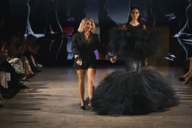 Ewa Minge wychodzi na finał pokazu Couture w Paryżu wraz z modelką prezentującą czarną kreację z tiulu.