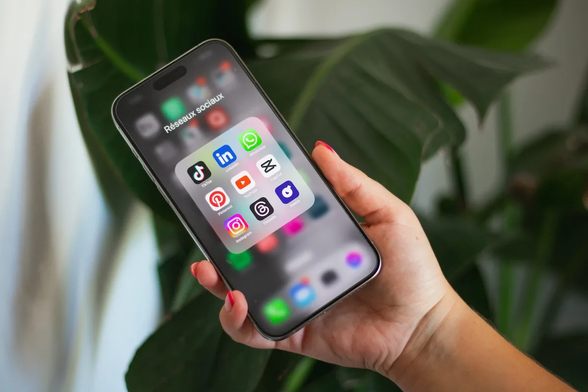 Francja zakaz mediów społecznościowych. Dłoń trzyma telefon z otwartym folderem „Réseaux sociaux”, w którym znajdują się m.in. TikTok, Instagram i YouTube – aplikacje objęte we Francji planowanymi ograniczeniami dla osób poniżej 15. roku życia.