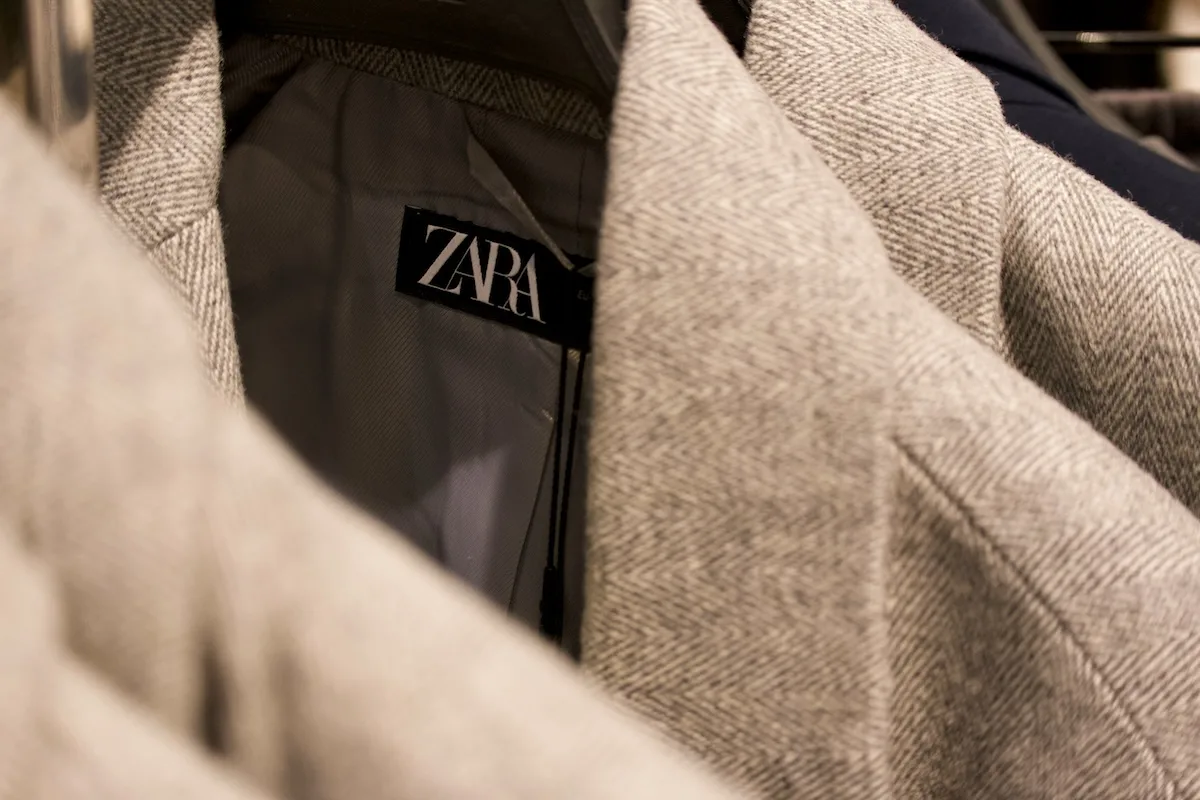 Zbliżenie na metkę Zara wszytą wewnątrz jasnej marynarki. Fotografia podkreśla detal produktu marki należącej do grupy Inditex.