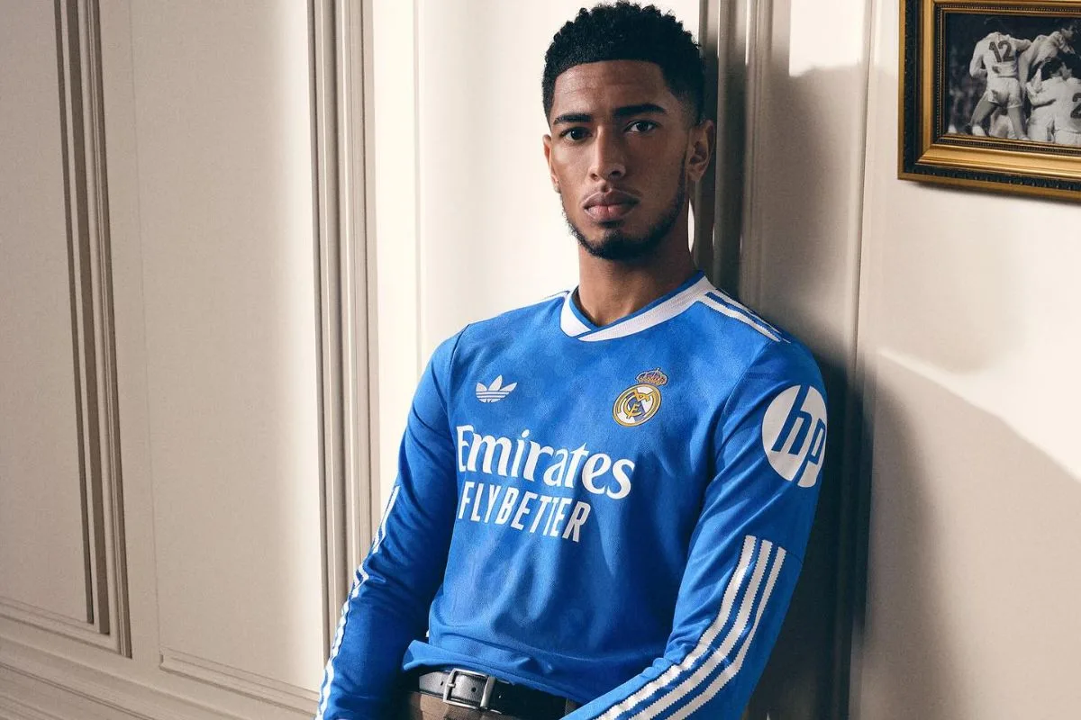 Jude Bellingham styl. Jude Bellingham pozuje we wnętrzu w niebieskiej koszulce Realu Madryt zaprojektowanej przez Adidas.