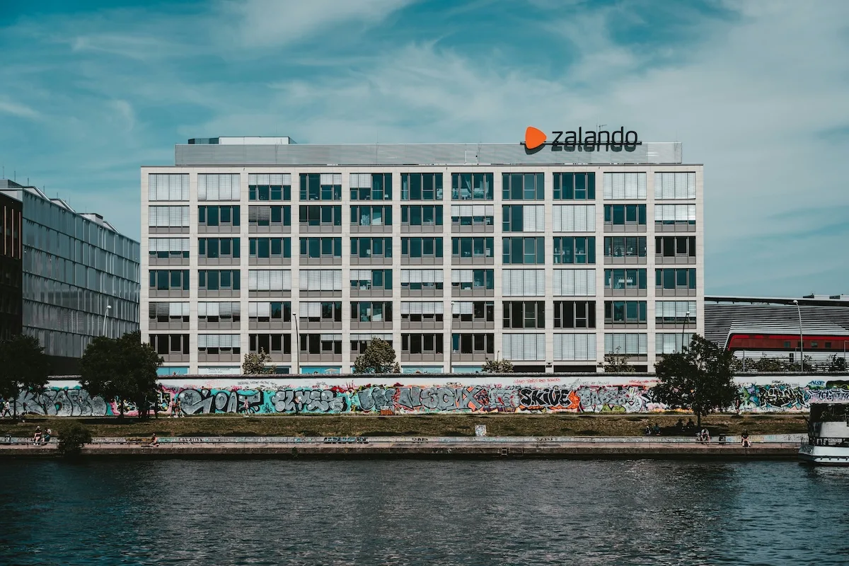 Zalando zwolnienia. Budynek biurowy Zalando w Berlinie widziany od strony rzeki, z logo marki na dachu. Firma reorganizuje struktury, redukuje zatrudnienie w Niemczech i jednocześnie rozwija nowe biuro w Rumunii.