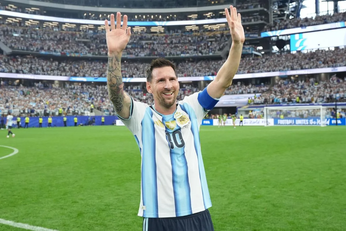 Biznesowe imperium Lionela Messiego. Na zdjęciu: Leo Messi w koszulce reprezentacji Argentyny z numerem 10 stoi na murawie i unosi obie ręce w geście pozdrowienia. Piłkarz uśmiecha się do kibiców zgromadzonych na wypełnionych trybunach stadionu. Zdjęcie podkreśla jego sportową rozpoznawalność oraz ogromny wpływ na zainteresowanie markami i produktami związanymi z jego nazwiskiem.