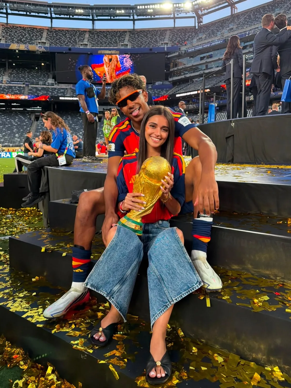 Inés García Santos i Lamine Yamal świętują na stadionie piłkarski sukces. Influencerka trzyma złote trofeum, a wokół pary widać konfetti i trybuny.
